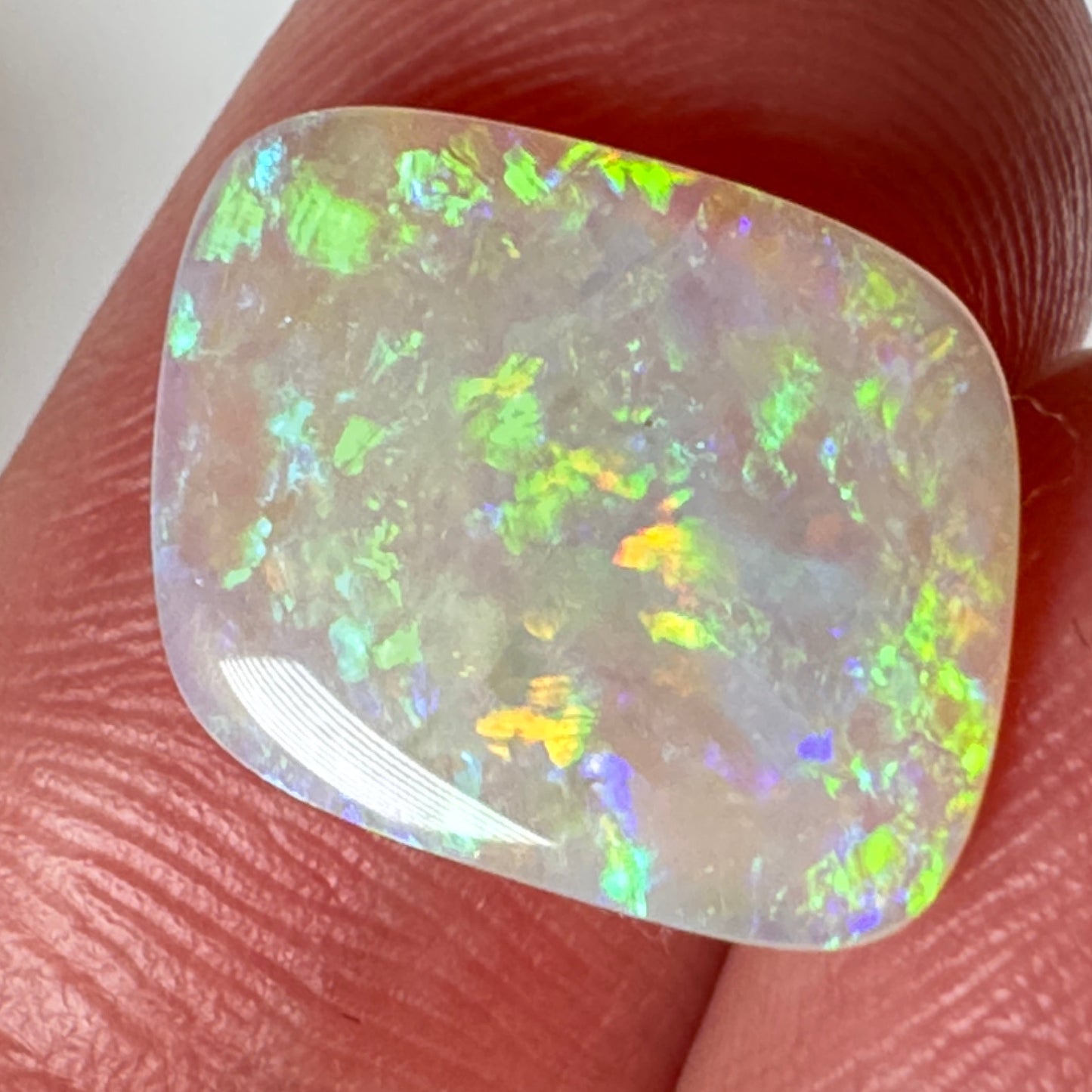 Opal gemstone held between fingers against a neutral background