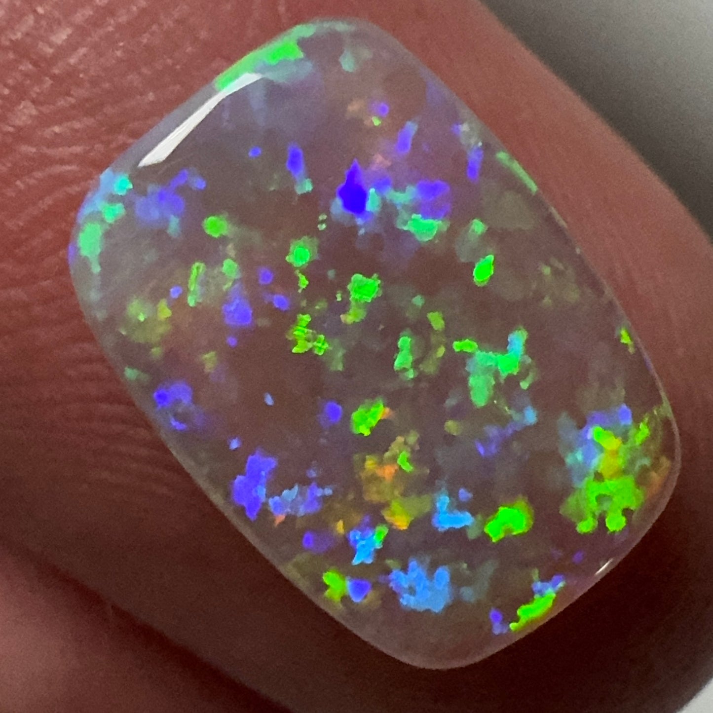 Opal stone held between fingers with a multicolored play of light.