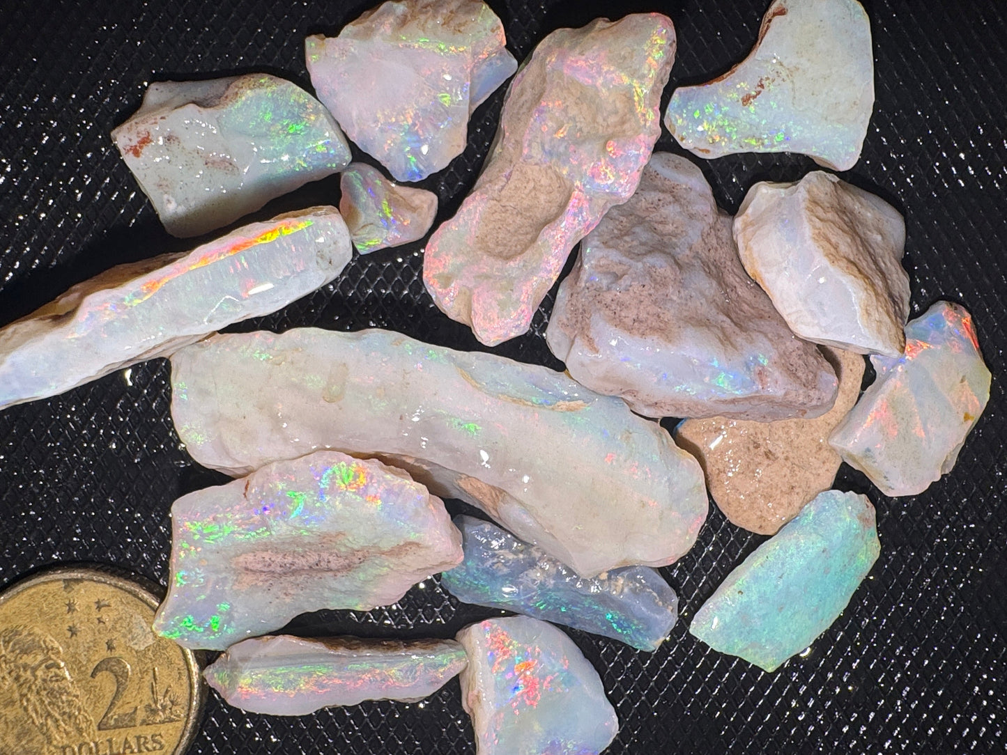 Raw opal stones on a black surface with a coin for scale.