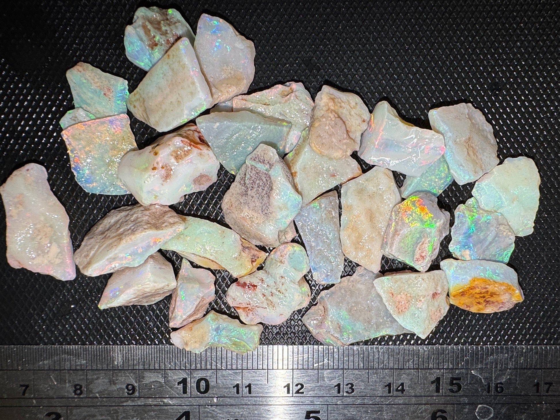 Raw opal stones on a black surface with a ruler for scale.