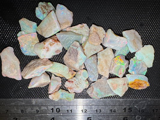 Raw opal stones on a black surface with a ruler for scale.