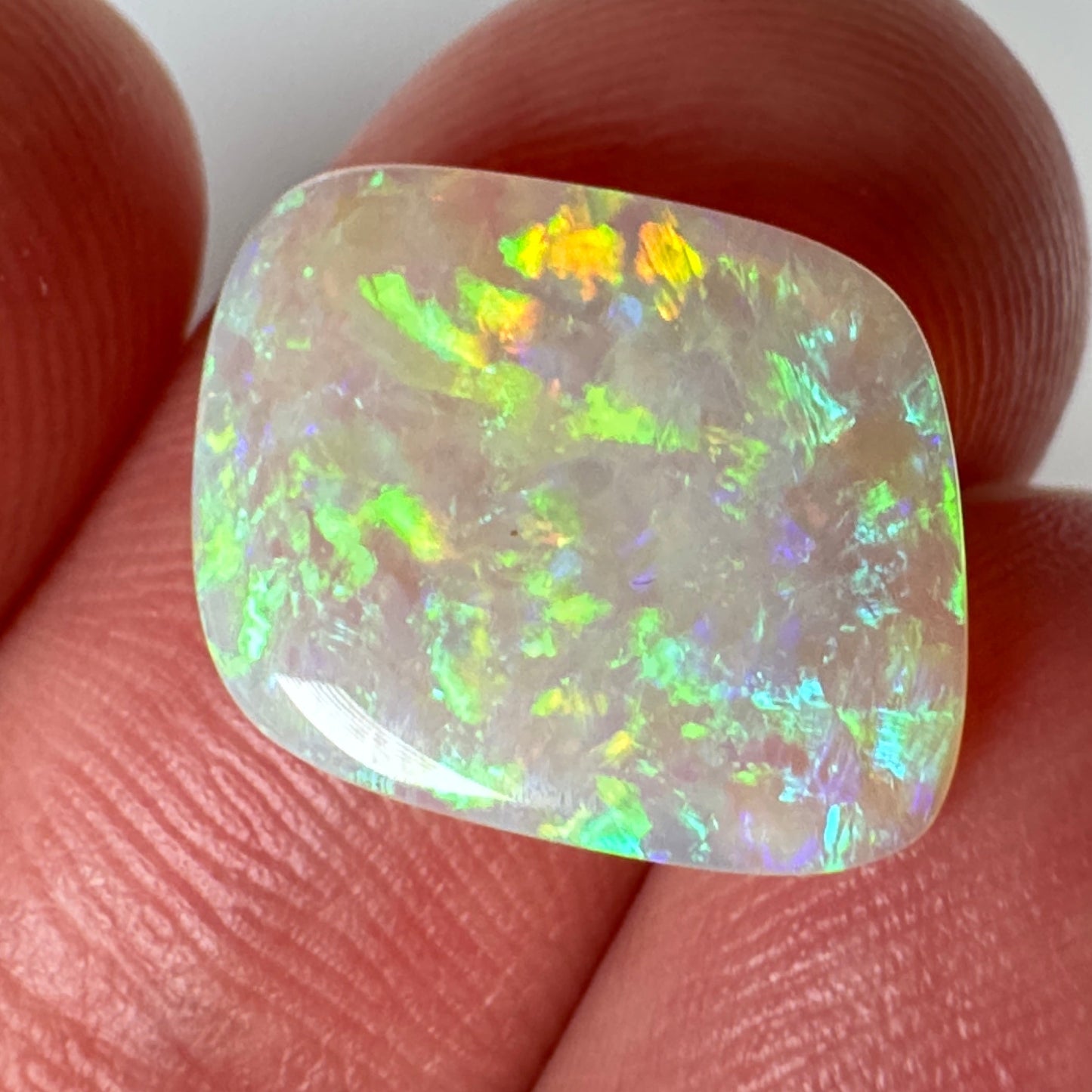 Opal stone held between two fingers against a white background