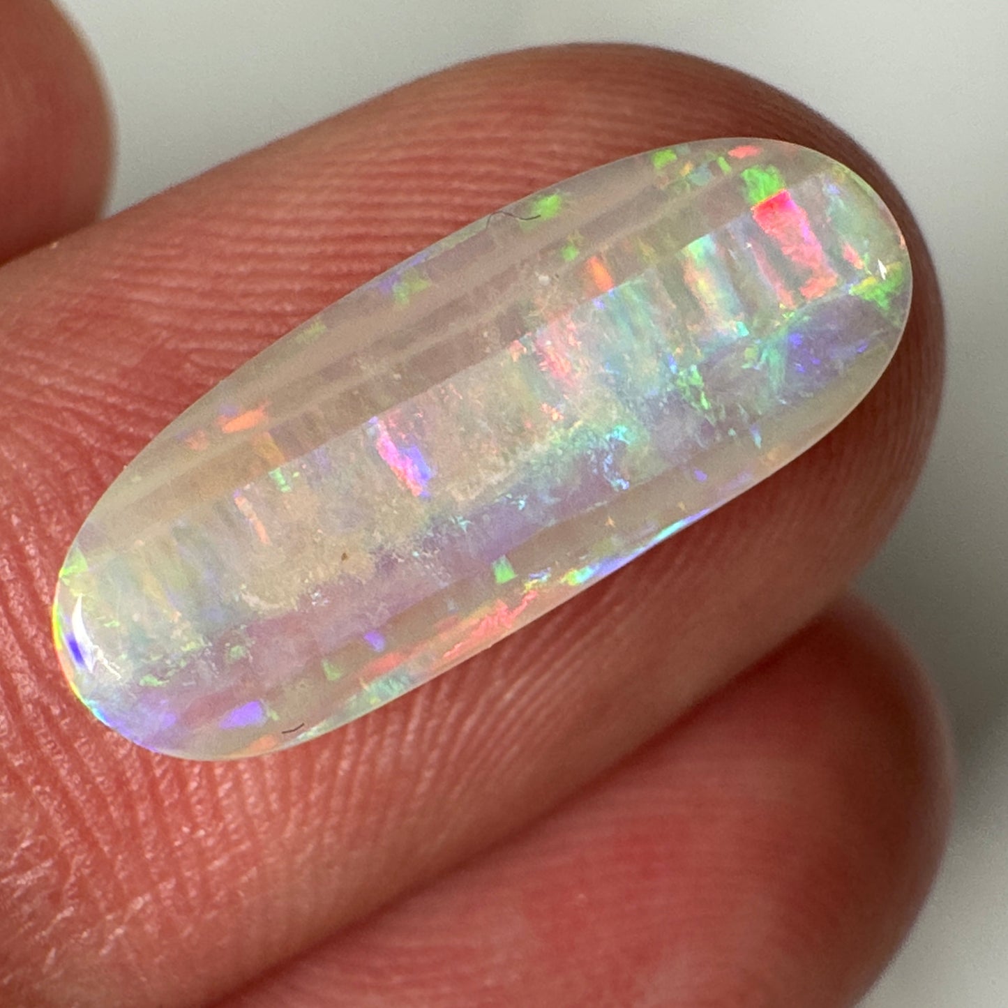 Opal stone held between fingers on a white background